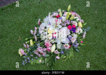 Eine Ansicht von oben eines bunten Beerdigungs-Kissenarrangements mit weißen Lilien, Rosen, Nelken und Chrysanthemen, das draußen ruhend platziert ist Stockfoto