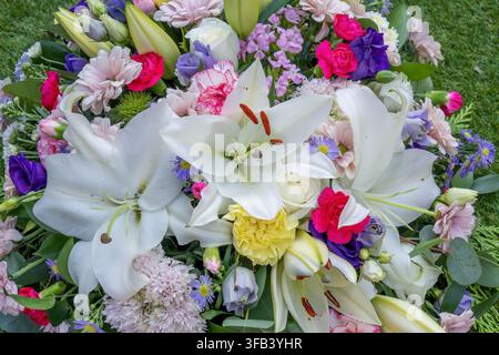 Eine detaillierte Vollbild-Aufnahme von oben eines Beerdigungsblumenarrangements mit auffälligen großen weißen Lilien, Rosen, Nelken und Tigergänseblümchen Stockfoto