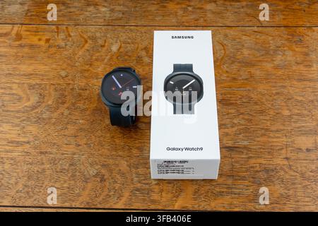 CHESTER, UK, 16. AUGUST 2026: Eine Aufsichtsfotografie einer Samsung Galaxy Watch 9 Smartwatch, die neben ihrer weißen Einzelhandelsverpackung auf einem Holztisch liegt Stockfoto