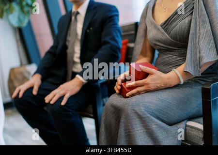 Elegantes Paar in formeller Kleidung, das rote Geschenkschachteln hält Stockfoto