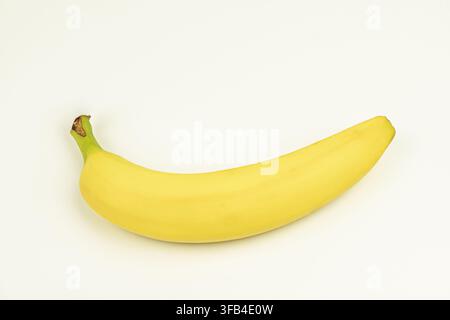 Reife Banane horizontal auf weißem Hintergrund positioniert, lebendige gelbe Farbe, grüner Stiel mit braunem Fleck, sauberer professioneller Stil, weiches gleichmäßiges Licht Stockfoto