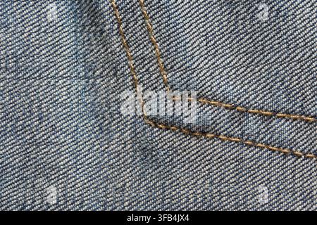 Blauer Denimstoff mit eckigen goldenen Nahtstichen, die den Rahmen füllen, zeigt diagonales Twillgewebe, Taschenrandkonstruktion und detaillierte Stoffoberfläche in Nahaufnahme. Stockfoto