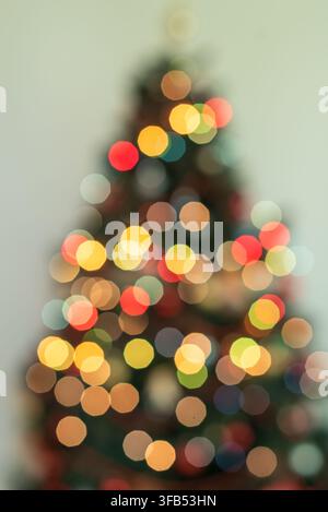 Elegante Weihnachtsbaum-Silhouette, umgeben von sanft verschwommenen warmen goldenen Lichtern vor einem hellen gelben Hintergrund, der eine festliche und gemütliche Atmosphäre schafft Stockfoto