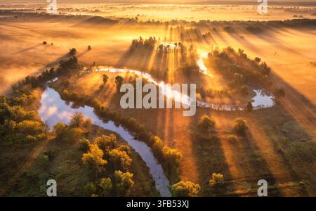 Luftbild eines sich windenden Flusses in goldenem Nebel mit Sonnenstrahlen. Sonnenaufgang Stockfoto