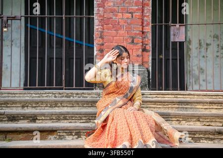 Eine Frau in traditioneller südasiatischer Kleidung sitzt auf Betonstufen und hält mit einer Hand ihr Kopftuch. Stockfoto