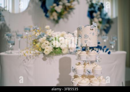 Elegante Hochzeitstorte und Cupcakes-Anzeige mit blauen und weißen Blumendekorationen Stockfoto
