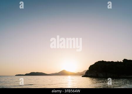 Geschmackvoller Küsten-Sonnenuntergang über ruhigem Meer und Hügeln Stockfoto