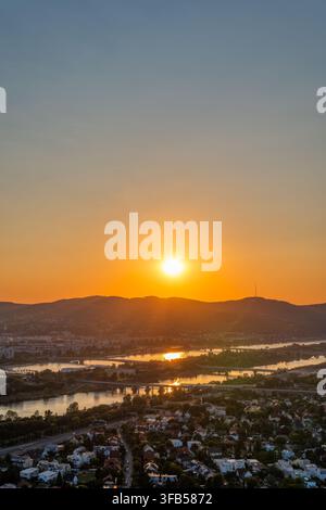 Goldener Sonnenuntergang über der Donau und grünen Hügeln in Wien aus der Vogelperspektive Stockfoto