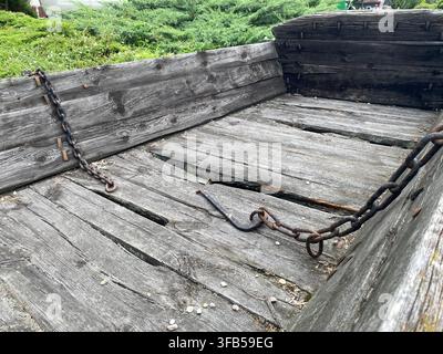 Verwittertes Holzfuhrwerk mit rostigen Ketten und Metallhaken im Freien, das gealterte Bretter und eine raue Textur zeigt Stockfoto
