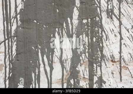 Graue Zement spritzer auf weißer Wand, Nahaufnahme von flüssigen Betontropfen auf rauer Putztextur, grunge architektonischer abstrakter Hintergrund. Stockfoto