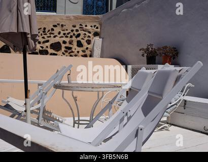 Weiße Loungestühle und Tisch auf einer Terrasse mit Vulkansteinmauer, Santorini, Griechenland Stockfoto