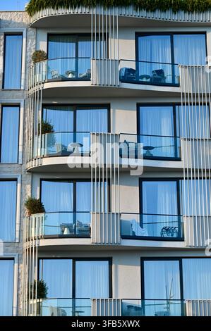 Eine architektonische Fotografie eines zeitgenössischen Wohngebäudexterieurs mit geschwungenen Glasbalkonen, großen Fenstern und vertikalen dekorativen Lamellen an einem sonnigen Tag Stockfoto