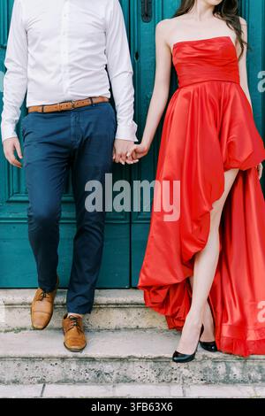 Elegantes Paar, das sich vor einer türkisfarbenen Tür an den Händen hält Stockfoto