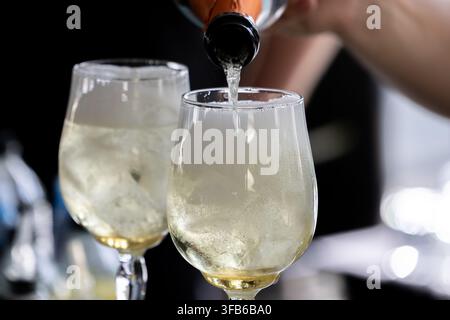 Schaumwein wird in mit Eis gefüllte Gläser gegossen. Blasen steigen während des Servierens im Getränk auf. Die Anordnung eignet sich für Catering und Gastronomie. Stockfoto