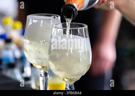 Schaumwein wird aus einer Flasche in Gläser gegossen. Blasen steigen im Getränk während des Servierens auf. Das Arrangement eignet sich für Catering und Gastronomie. Stockfoto