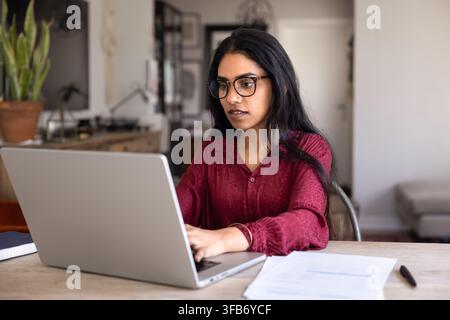 Junge Frau sitzt am Tisch und arbeitet an einem Laptop im Homeoffice Stockfoto
