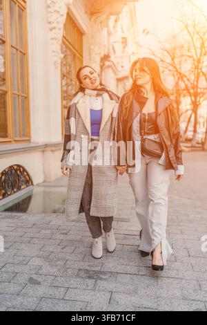 Frauenfreunde gehen zusammen eine historische Stadtstraße entlang während der goldenen Stunde und tragen stilvolle Herbstmode Stockfoto