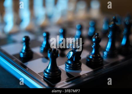Ein Schachspielstein auf einem digitalen Schachbrett mit blauer Beleuchtung und geringer Schärfentiefe, der eine dramatische Strategiespielszene mit reflektierenden schwarzen Figuren erzeugt Stockfoto