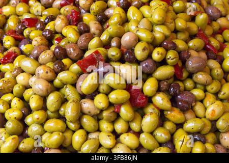 Eine große, farbenfrohe Auslage mit gemischten grünen und schwarzen Oliven, mariniert mit Kräutern und Stücken roter Chilipeper, auf einem Freiluftmarkt in Frankreich. Stockfoto