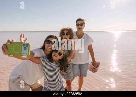 Glückliche multigenerationale Familie, die ein Selfie mit dem Smartphone im seichten rosa Salzwasser macht. Mutter, Großmutter, zwei Kinder lächeln, winken Stockfoto