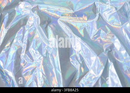 Nahaufnahme von zerknittertem holografischem Stoff mit weichem metallischem Schimmer und wechselnden pastellfarbenen Regenbogenreflexionen, der abstrakte Falten und leuchtenden Text bildet Stockfoto