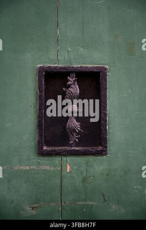 Schwarzes schmiedeeisernes Fenstergitter auf einem rissigen grünen Holztürhintergrund. Stockfoto