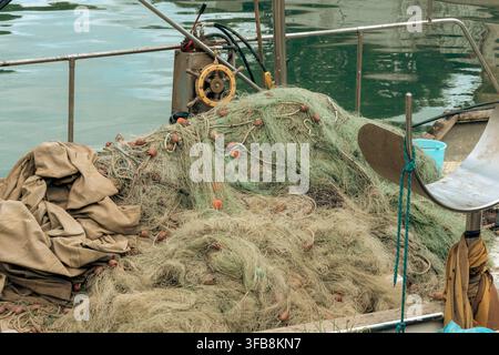 Ein großer Haufen Fischernetze ruht auf einem Bootdeck neben ruhigem grünem Wasser. Stockfoto