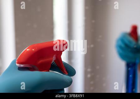 Nahaufnahme einer Hand, die einen blauen Schutzhandschuh trägt und eine rote Sprühdose mit Auslöser hält, bereit zum Reinigen Stockfoto
