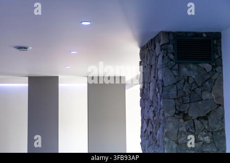Ein zeitgenössischer Innenraum mit einer texturierten Steinsäule, einer schlanken Decke mit Einbauleuchten und ambienter LED-Beleuchtung Stockfoto