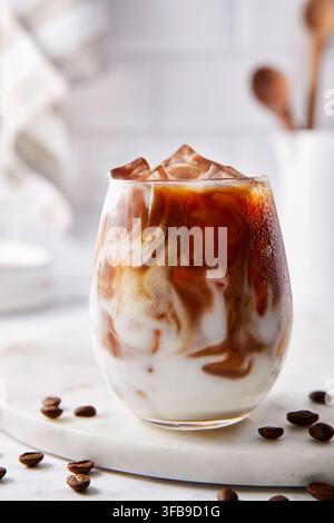 Eiskalter Caffè Latte. Dunkler Kaffee gemischt mit Milch und Eiswürfeln. Helle Beleuchtung in der Küche. Stockfoto