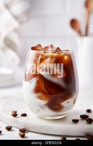 Eiskalter Caffè Latte. Dunkler Kaffee gemischt mit Milch und Eiswürfeln. Helle Beleuchtung in der Küche. Stockfoto