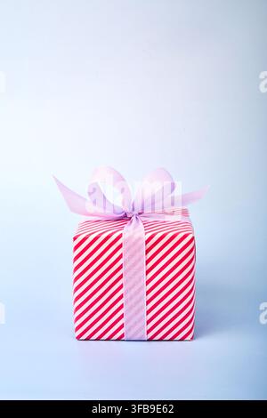 Geschenk in rosa gestreiftem Papier mit einer lila Schleife verpackt. Hellblauer Hintergrund. Geburtstagsgeschenk. Stockfoto