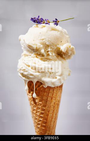 Löffel Vanilleeis in einer Waffel. Ein Lavendelblüte ruht auf dem Eis. Das Eis tropft an der Seite der Waffel herunter. Helles Licht Stockfoto