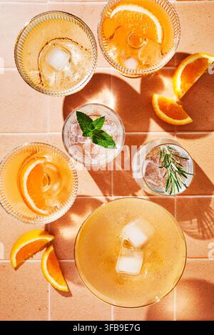 Verschiedene Gläser gefüllt mit erfrischenden Sommergetränken auf gelben Fliesen. Orangenscheiben, Minzblätter, Rosmarin und Eiswürfel. Sonnenlicht. Stockfoto