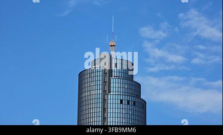 Der obere Teil eines markanten, gestuften Hochhauses aus dunklem Glas mit einem hohen orange-weißen Funkkommunikationsmast vor einem blauen Himmel Stockfoto