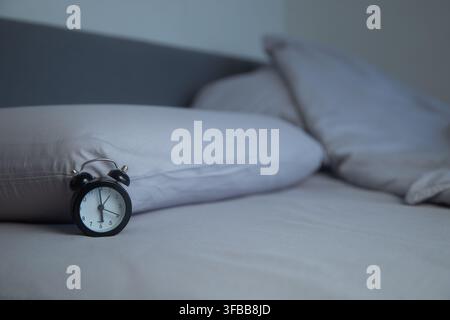 Auf dem hellgrauen Bettlaken liegt eine schwarze Miniaturwecker vor dem Hintergrund von zwei Stockfoto