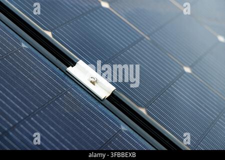 Detaillierte Ansicht von Photovoltaikzellen und ihren Verbindungsgitterlinien, die eine Metallklemme hervorhebt, die das Panel an einem dunklen Schienenprofil befestigt Stockfoto