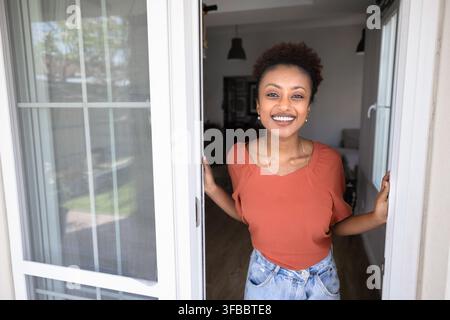 Lächelnde afrikanische Frau steht auf der Hausveranda und schaut in die Kamera Stockfoto
