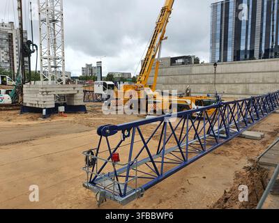 Eine Baustelle mit schweren Maschinen, darunter ein großer gelber mobiler Kran, der auf matschigem Boden steht. Im Vordergrund ein blauer Stahl Stockfoto