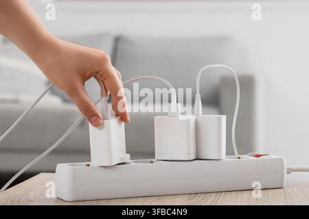 Energieverbrauch und Stromüberlastung, Hand steckt Ladegerät in Steckdosenleiste mit mehreren Geräten Stockfoto