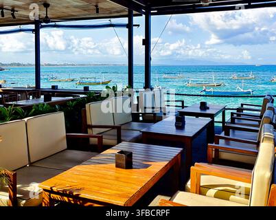 Freiluft-Strandcafé mit Meerblick und traditionellen Auslegerbooten (jukung), die im Meer vor Anker liegen, Bali, Indonesien Stockfoto