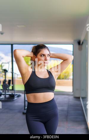 Junge Frau streckt ihre Arme hinter dem Kopf in einem modernen Fitnessstudio Stockfoto