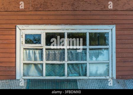 Altes Holzfenster an einem rustikalen Landhaus mit verwittertem Rahmen. Vintage-Ländliche Architektur im natürlichen Tageslicht. Stockfoto