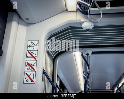 Innenraum einer Straßenbahn mit Verbotssymbolen für das Fahrgastverhalten neben CCTV-Überwachungskameras, Handläufen und Gelenkabschnitten, die verwendet werden Stockfoto
