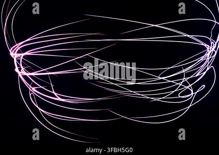 Abstrakte Lichtmalerei-Fotografie mit leuchtenden rosa und weißen Streifen, die dynamische gebogene Linien gegen einen einheitlichen dunklen Hintergrund bilden. Stockfoto
