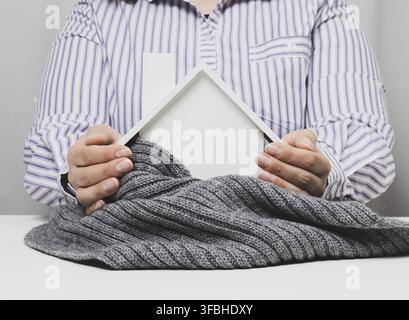 Weibliche Hände zusammengefaltet über einem hölzernen Modellhaus auf weißem Hintergrund. Immobilienversicherungskonzept, Umweltschutz, Stockfoto