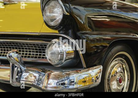 Detaillierte Nahaufnahmen mit niedrigem Winkel heben die Vorderseite eines Oldtimers in auffälliger Gelb- und Schwarzfarbe hervor. Polierte Chromelemente glänzen, reflektieren Stockfoto