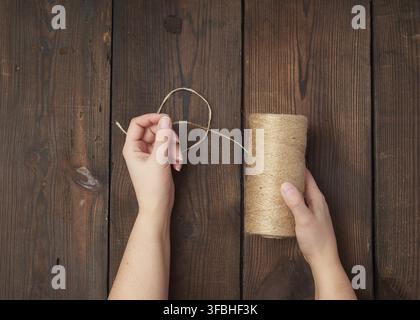 Weibliche Hände halten ein Strang mit braunen eco Thread auf braunem Holz- Hintergrund, Ansicht von oben Stockfoto
