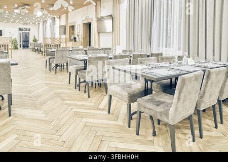 Seitenansicht eines großen, hellen, leeren Restaurants mit Tischen, weichen Stühlen, Vorhängen und einem Holzboden. Modernes Interieur eines Cafés, Restaurants für Veranstaltungen Stockfoto