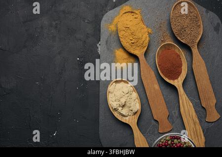 Bunte gemahlene Gewürze in Holzlöffeln auf einem schwarzen Brett, Kopierraum Stockfoto